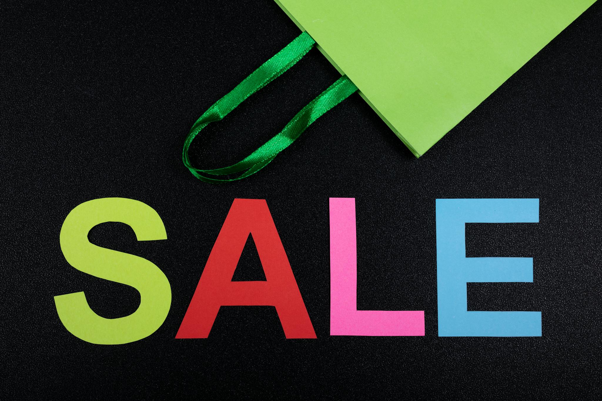Close-up of colorful SALE letters on black background with green shopping bag.
