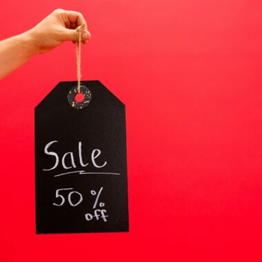 Hand holding a black sale tag with 50% off on a vibrant red background.